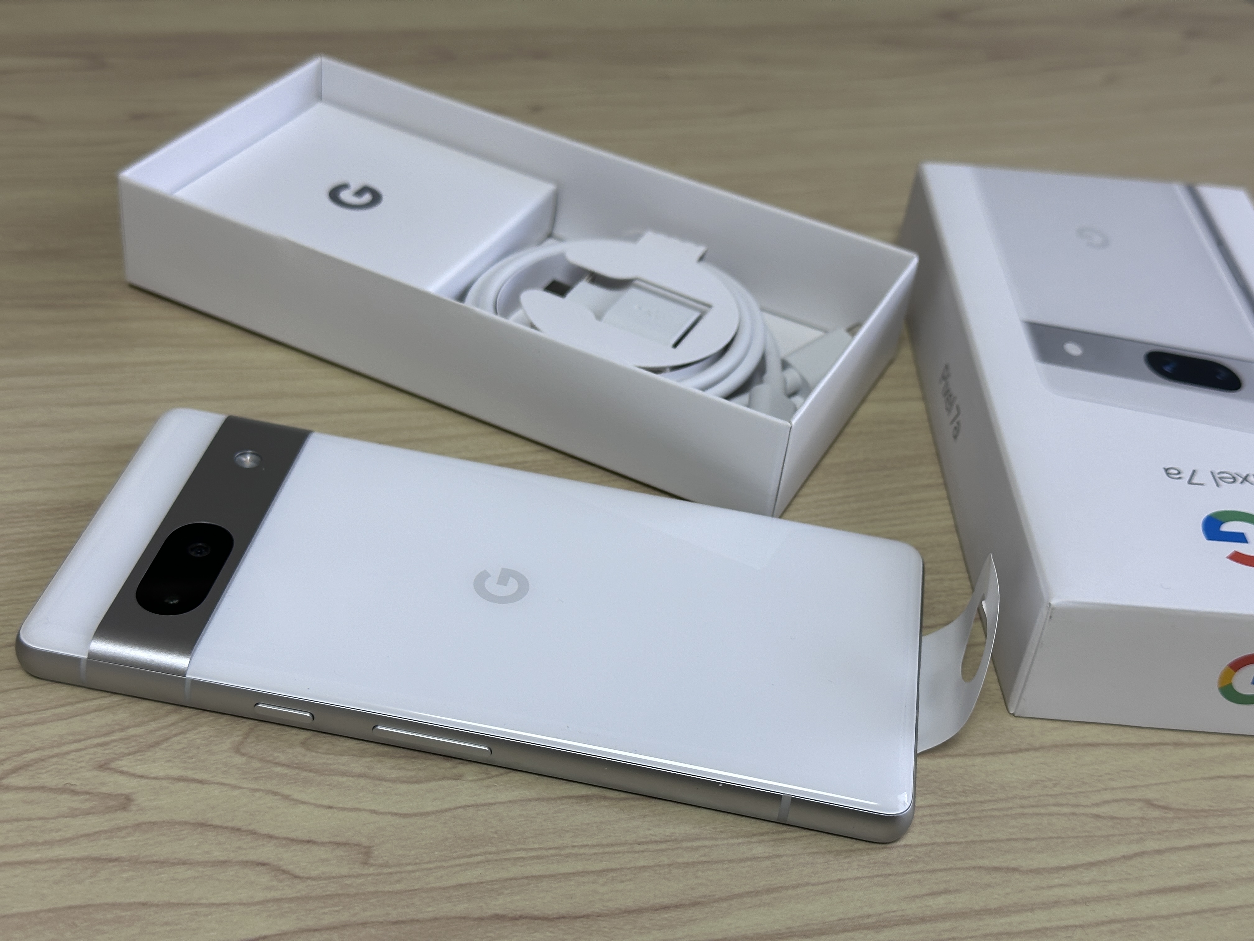 明るい色のPixel 7a背面と箱・USB-Cケーブル。正式色名、地域版や販売品の付属品は写真だけでは分からない